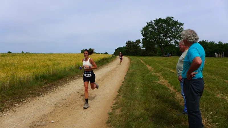 Une traileuse sur un chemin de terre bordé de champs de blé, encouragée par des bénévoles